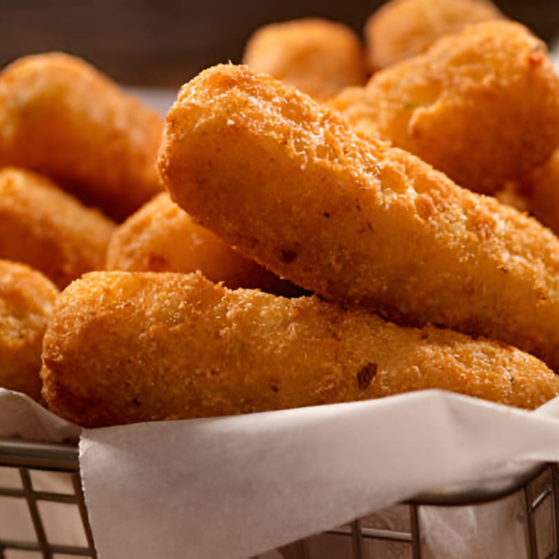 Close-up of golden-brown fried mozzarella sticks in a metal basket lined with white paper.