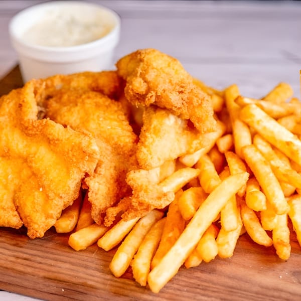 Golden fried fish and french fries on a wooden board with a side of tartar sauce.