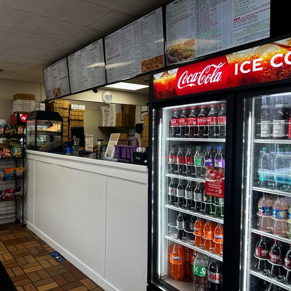 Interior view of Apollon Roast Beef & Pizza, showing menu boards, a counter, and a Coca-Cola fridge.