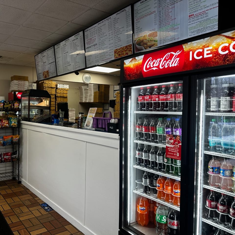 Interior view of Apollon Roast Beef & Pizza, showing menu boards, a counter, and a Coca-Cola fridge.
