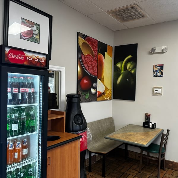 A corner of Apollon Roast Beef & Pizza dining area with a soda fridge, table, and food art.