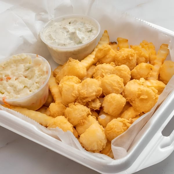Fried scallops and french fries with coleslaw and tartar sauce in a white takeout container.