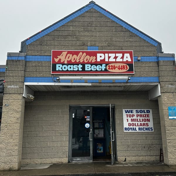 Exterior of Apollon Roast Beef & Pizza, a gray brick building with a red and blue sign.