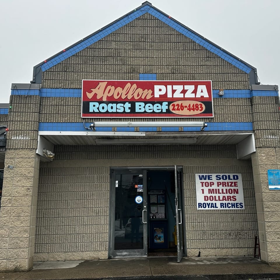 Exterior of Apollon Roast Beef & Pizza, a gray brick building with a red and blue sign.