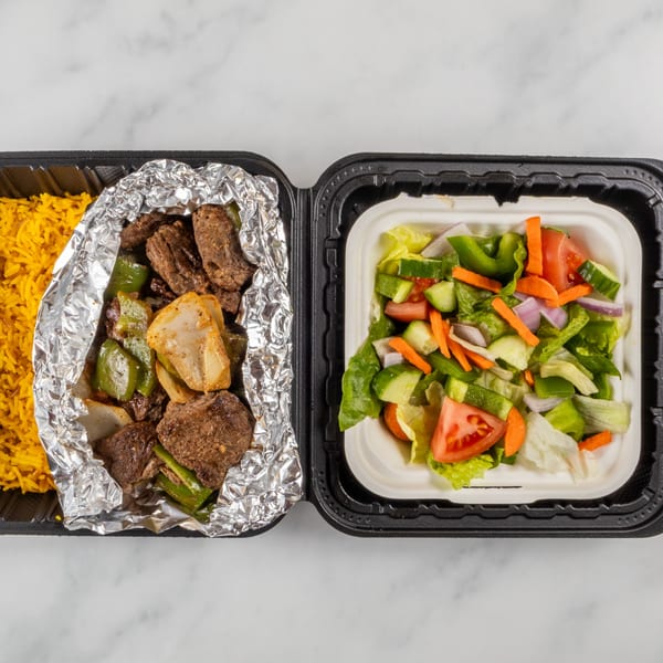 Takeout container with yellow rice, beef and peppers in foil, and a fresh garden salad.