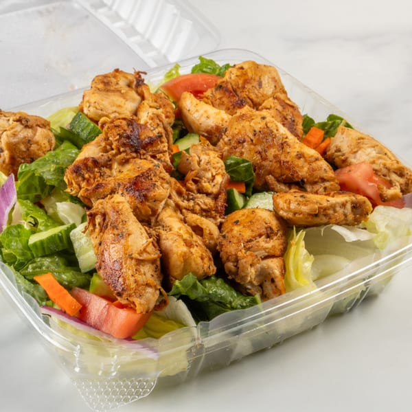 Grilled chicken salad with lettuce, tomatoes, cucumbers, and red onion in a clear plastic container.