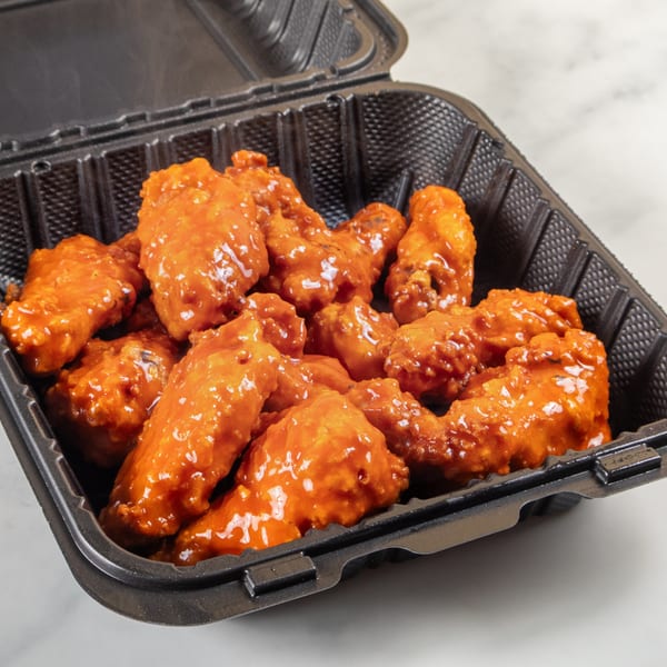 Buffalo chicken wings, coated in a glossy orange sauce, in a black takeout container.